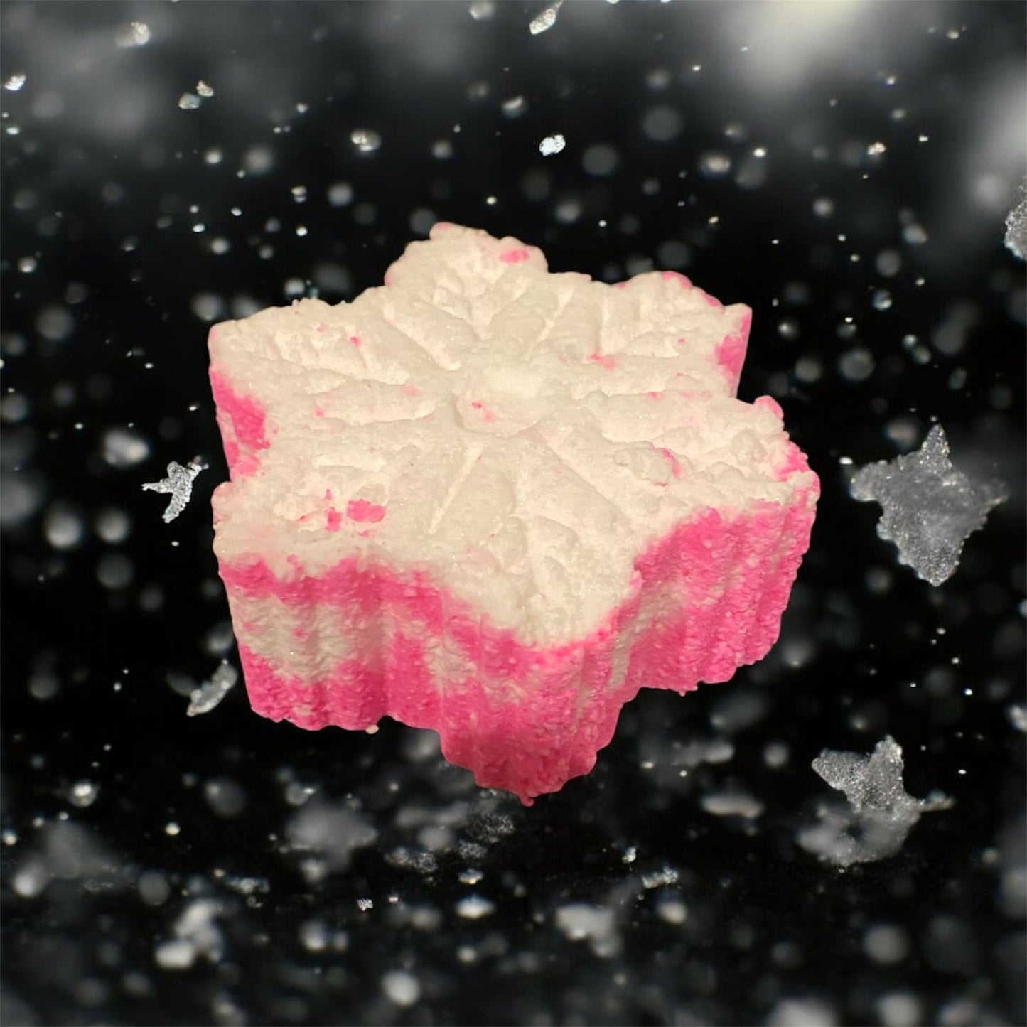 A pink and white snowflake shaped bath bomb with a dark snowy background