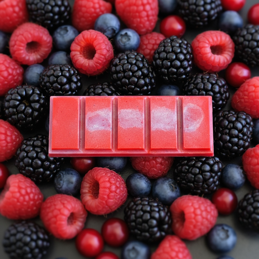 A rectangular red, pink and purple wax bar with five segmented pieces, placed on top of a dense mix of fresh raspberries, blackberries, blueberries, and red cherries.