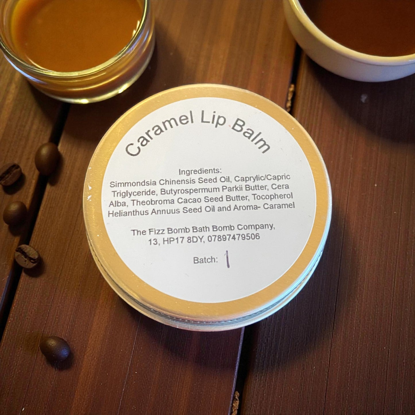 Caramel lip balm container with ingredients list on a wooden surface