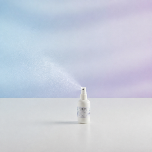 A white spray bottle labeled 'CLEAN' with a fine mist spraying out, set on a white surface against a soft blue and purple gradient background.