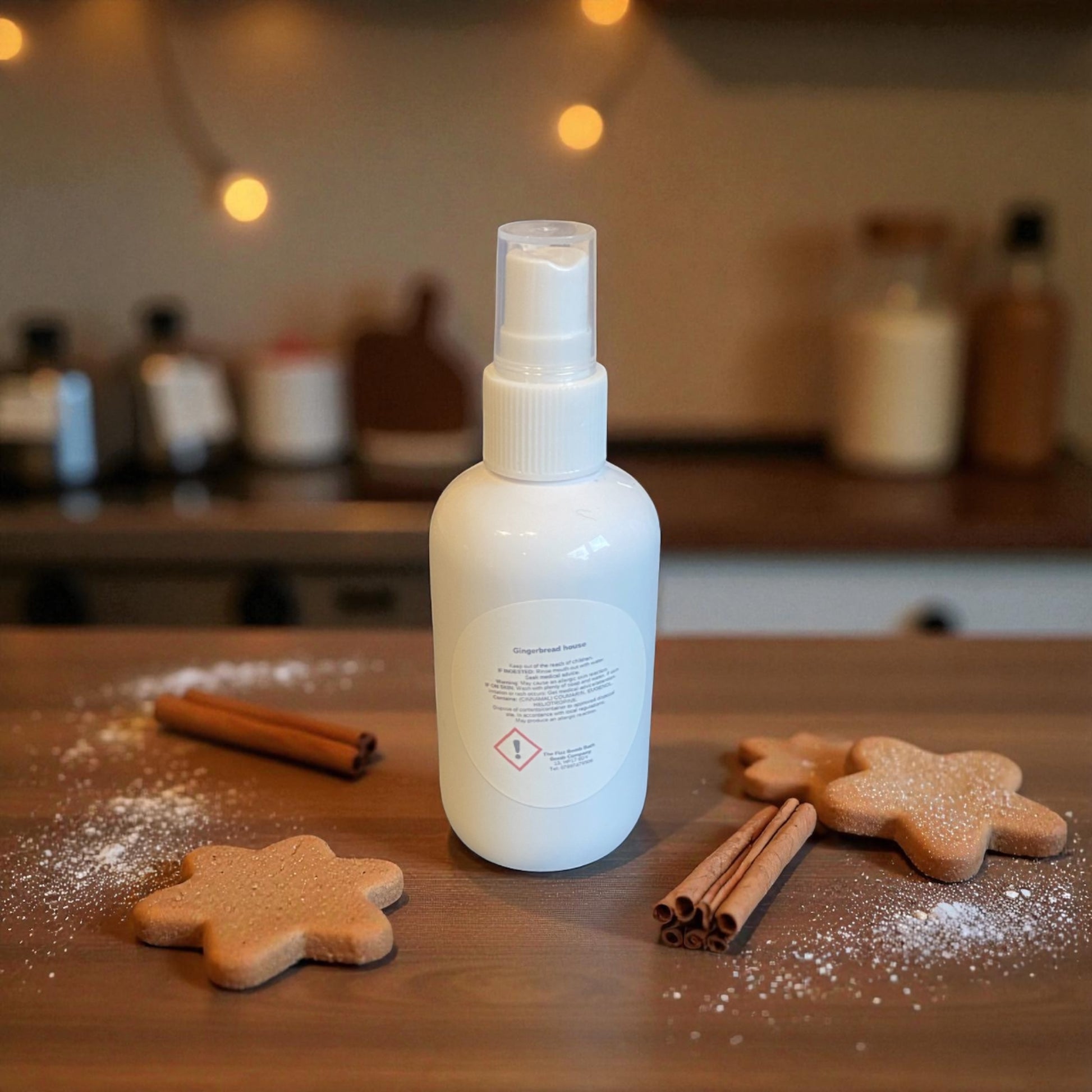 White spray bottle on a wooden surface with gingerbread cookies and cinnamon sticks, blurred kitchen background
