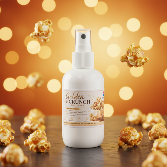 A white spray bottle labeled 'Golden Crunch Body Spray' stands on a dark wooden surface with scattered caramel popcorn around it and a warm orange bokeh background.
