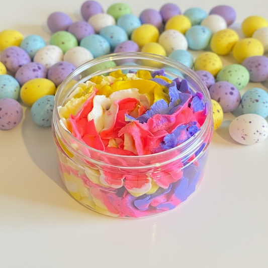 A multi coloured whipped soap in a jar with mini eggs background
