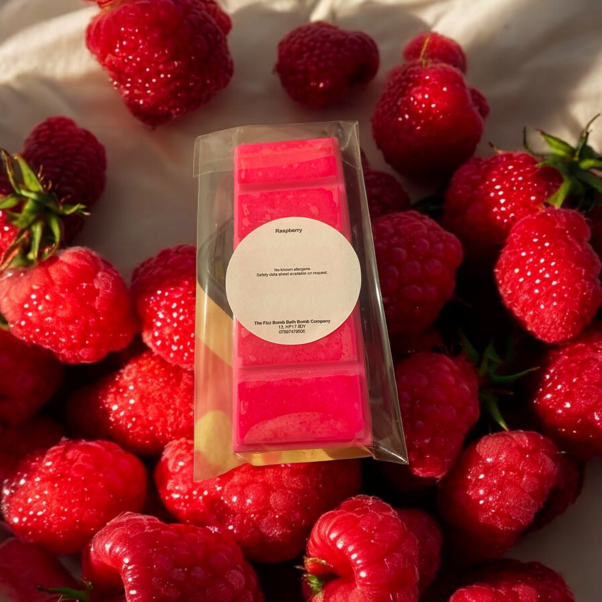 Packaged wax melts surrounded by raspberries on a white background