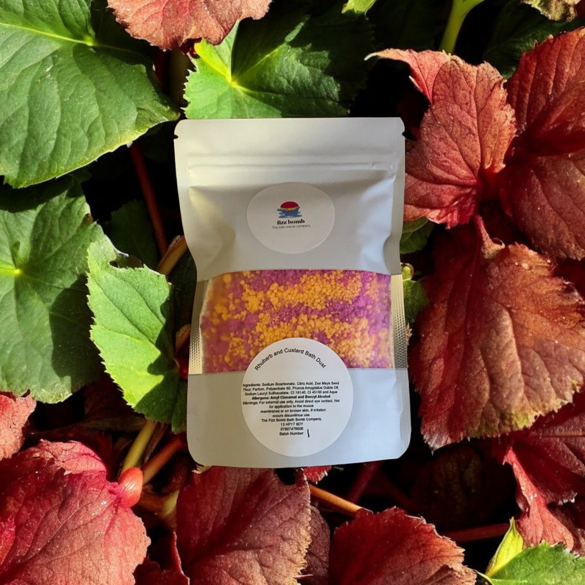 A packet of yellow and pink rhubarb and custard scented bath dust with a background of rhubarb leaves