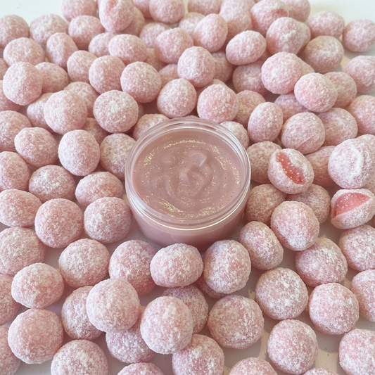 A light pink coloured hair mask in a pot with a strawberry Bon Bon sweets background.